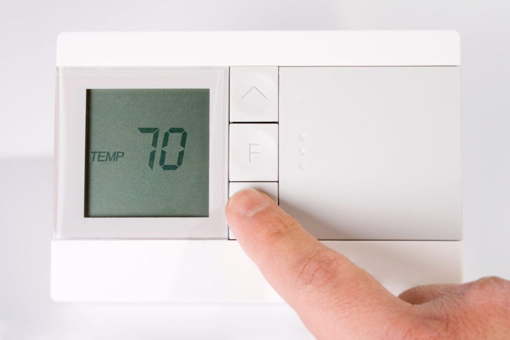 Home thermostat set to 70 degrees and a finger in the frame lowering the temperature.
